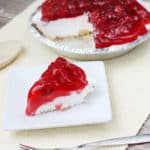 No bake cherry cheesecake slice on a white plate in front of the whole pie in the background