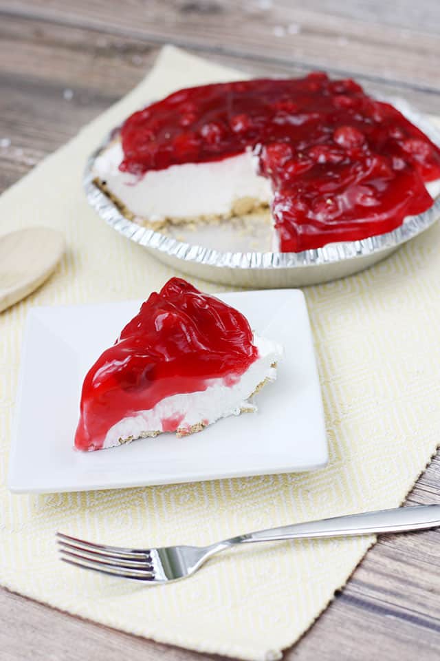No bake cherry cheesecake slice on a white plate in front of the whole pie in the background
