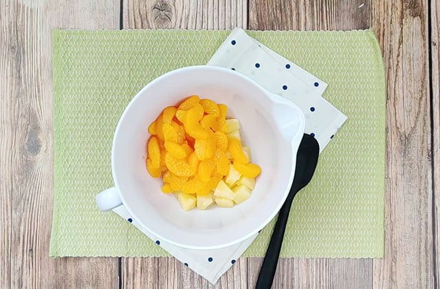 Mandarin oranges and pineapple chunks in a white mixing bowl