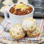 Beer bread muffins stacked next to a bowl of chili on a placemat