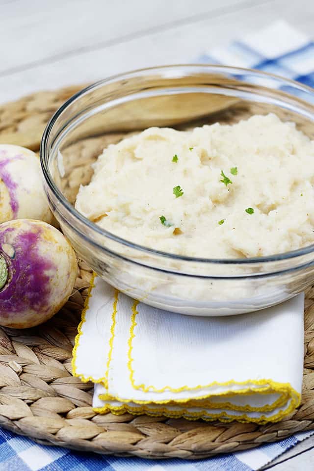 Mashed turnips in a glass bowl next to whole turnips