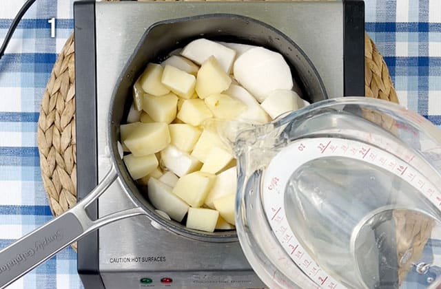 Pouring water over chopped turnips and potatoes in a saucepan on a stove top