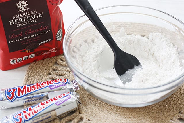 A glass bowl of dry ingredients for brownies with a black spatula