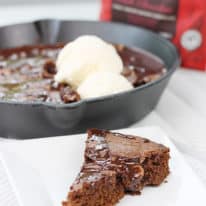 A slice of the brownie skillet on a white square plate with the cast iron skillet in the background