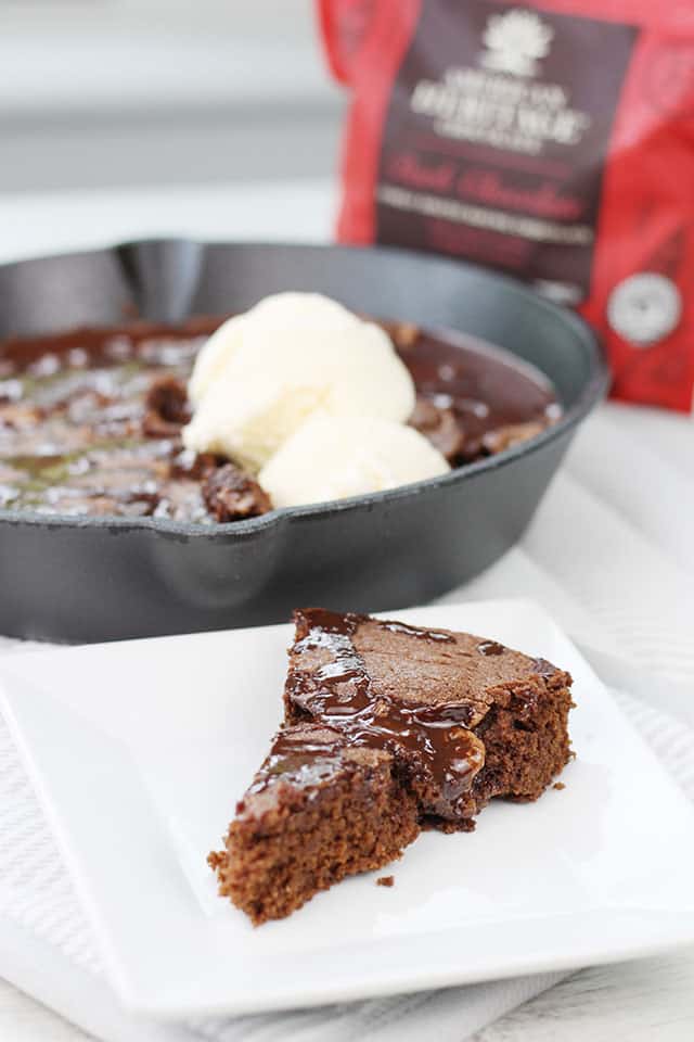 A slice of the brownie skillet on a white square plate with the cast iron skillet in the background