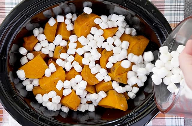 Sprinkling miniature marshmallows on top of sweet potatoes in a Crockpot